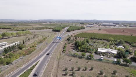 Cars-exiting-a-traffic-circle-roundabout-on-their-way-to-entering-the-town,-Aerial-approach-shot