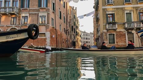 Low-angle-water-surface-pov-of-boat-passing-with-tourists-on-board-and-rowing-man-standing,-hanging-sheets-in-background