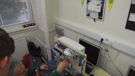 Adult-male-teacher-helping-a-young-student-build-an-electrical-switch-board-at-vocation-high-school