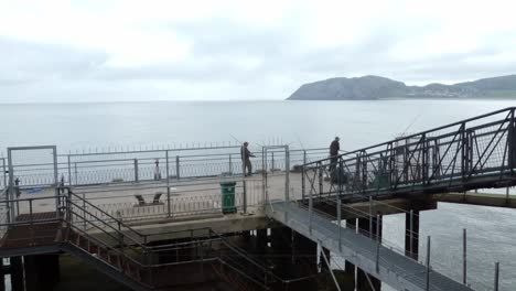 Males-with-fishing-rods-angling-on-Llandudno-pier-jetty-preparing-equipment-and-waiting-in-anticipation