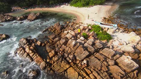 Aerial-FPV-shot-of-man-standing-in-the-rocks-island-in-between-the-sea