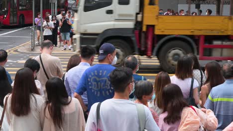 Asian-pedestrians-and-commuters-wait-on-the-sidewalk-for-a-traffic-light-signal-to-turn-green-as-vehicles-drive-through-before-rushing-and-walking-a-busy-zebra-crossing-junction