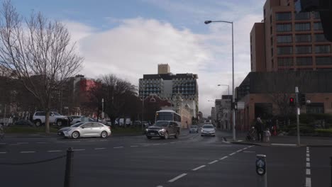 Vea-La-Calle-Campbell-En-Hobart,-Mientras-Los-Autos-Conducen-Por-Una-Carretera-Mojada-Con-El-Hospital-Al-Fondo,-Los-Peatones-Esperan-En-Las-Luces-Para-Cruzar-La-Calle-En-Un-Día-Claro-De-Invierno