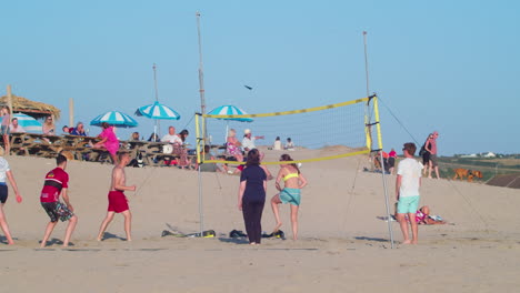 Gente-Jugando-Voleibol-En-La-Playa-En-Verano,-Mujer-Atlética-Salta-Y-Lanza-La-Pelota-Sobre-La-Red