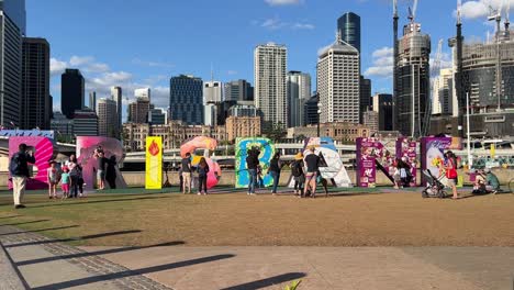 Fröhliche-Menschen,-Die-Spaß-Daran-Haben,-Das-Blockschild-Von-Brisbane-Hinaufzuklettern-Und-An-Einem-Sonnigen-Tag,-Queensland,-Australien,-Das-Berühmte-Wahrzeichen-Der-Stadt-Mit-Dem-Modernen-Stadtbild-Der-Innenstadt-Im-Hintergrund-Zu-Fotografieren