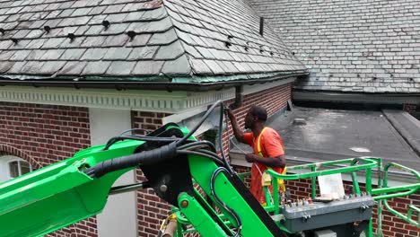 Orbit-aerial-shot-of-African-American-worker-spray-painting-touch-ups-on-brick-building