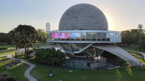 Carretilla-Aérea-Del-Planetario-Galileo-Galilei-Y-Gente-Descansando-En-Los-Bosques-De-Palermo-Al-Atardecer,-Buenos-Aires