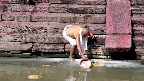 Old-Man-Bending-Down-While-Cleaning-Dish-Pan-In-The-Bagmati-River-Near-Pashupatinath-Temple-In-Kathmandu,-Nepal