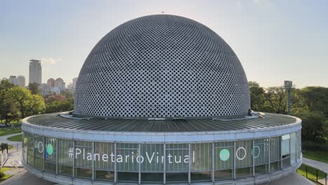 Aerial-dolly-out-of-Galileo-Galilei-Planetarium-in-Palermo-Woods,-skyline-in-background-at-daytime,-Buenos-Aires