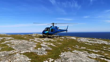 Privathubschrauber-Thront-Auf-Dem-Gipfel-Einer-Bergklippe-Mit-Blick-Auf-Die-Landschaft-Des-Blauen-Ozeans-Und-Mit-Weitem-Propellerdrehwinkel