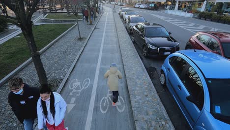 Luftaufnahme-Eines-Kindes,-Das-Spaß-Beim-Rollerfahren-Entlang-Des-Fahrradwegs-Am-Wasser-Von-Arona-In-Italien-Hat