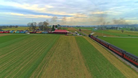 Una-Vista-Aérea-De-Un-Antiguo-Tren-De-Vapor-Restaurado-Y-Vagones-De-Pasajeros-Que-Siguen-Con-Humo-Y-Vapor-Con-Turistas-Y-Espectadores-Viendo-Como-Los-Ve-Un-Dron