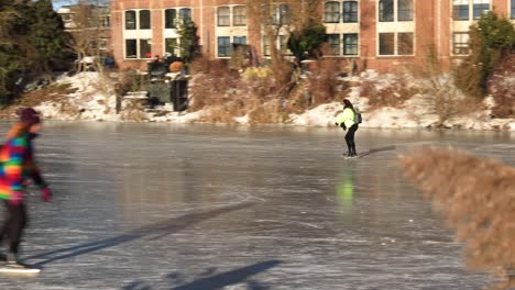 Follow-movement-of-ice-skating-people-on-the-canal-with-reed-in-the-foreground-revealing-historic-medieval-buildings-of-Drogenapstoren-and-Walburgiskerk-in-the-background