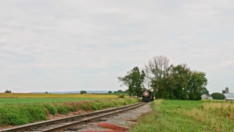 Una-Antigua-Locomotora-Restaurada-Y-Vagones-De-Pasajeros-Acercándose-En-Un-Día-Nublado-Viajando-Por-El-Campo