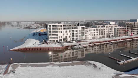 Descenso-Aéreo-De-Noorderhaven-Y-Acercamiento-De-Un-Nuevo-Edificio-De-Apartamentos-De-Lujo-Contemporáneo-En-Un-Paisaje-Urbano-De-Nieve-Brillante-Reflejado-En-El-Alto-Nivel-Del-Agua-En-El-Puerto-Recreativo-En-Primer-Plano