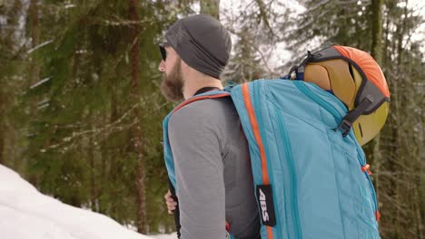 Athletic-bearded-man-hiking-in-snow-forest-with-poles-and-backpack