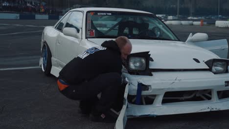 Hombre-Haciendo-Reparaciones-En-Un-Auto-A-La-Deriva-Dañado,-Plano-Amplio-De-La-Plataforma-Rodante-A-La-Derecha