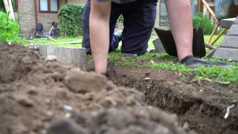 Gardener-Building-Stone-Slab-Wall-Around-Vegetable-Garden,-Low-Angle