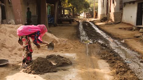 Indian-woman-with-head-covered-by-traditional-pink-veil-looking-at-camera-and-smiling-while-kneading-mortar-or-sand,-India