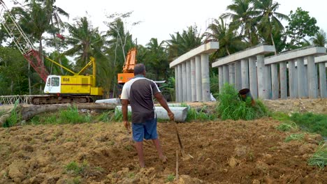 Granjero-Solitario-De-Indonesia-Cavando-Suelo-Con-Máquinas-Industriales-Masivas-En-El-Fondo