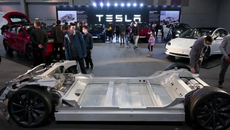 Los-Visitantes-Miran-Un-Automóvil-Con-Chasis-De-Motor-Tesla-Y-El-Bastidor-De-Un-Vehículo-De-Motor,-Durante-La-Exposición-Internacional-Del-Motor-Que-Exhibe-Automóviles-Eléctricos-Ev-En-Hong-Kong