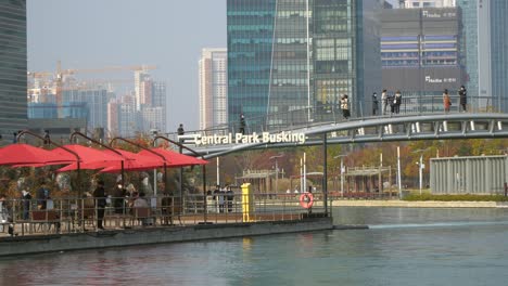 Korean-people-in-face-masks-relaxing-in-Songdo-Central-Park-Busking-area-and-sightseeing-views-from-footbridge-over-the-lake-in-Incheon,-South-Korea