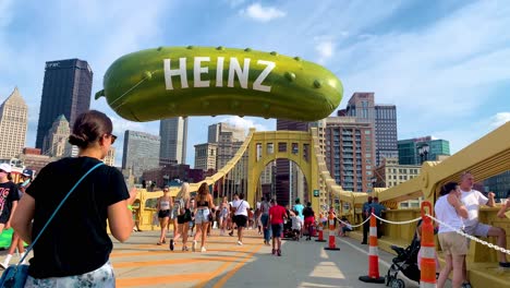 Menschen,-Die-Auf-Der-Andy-Warhol-Brücke-Laufen,-Mit-Einem-Riesigen-Heinz-Pickle-Ballon-Im-Hintergrund