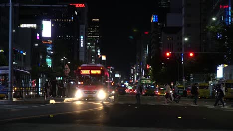 Muchas-Personas-Que-Usan-Máscaras-Protectoras-Durante-La-Pandemia-De-Covid-19-Cruzan-La-Calle-En-La-Parada-De-Autobús-De-La-Calle-Gangnam-En-La-Noche-De-Seúl,-Corea-Del-Sur