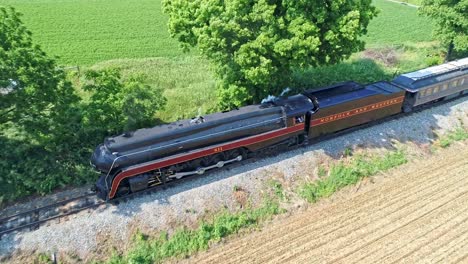 An-Aerial-View-of-a-Steam-Engine-Puffing-Smoke-and-Steam-with-Passenger-Coaches-Traveling-on-a-Single-Track-Thru-Trees-and-Farmland-Countryside-on-a-Beautiful-Cloudless-Spring-Day