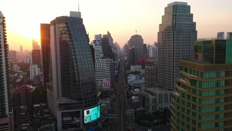 Epic-aerial-flying-through-skyline-and-skyscrapers-of-Sukhumvit-district-during-sunrise-in-Bangkok,-Thailand