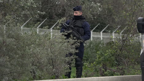 Un-Oficial-De-Policía-De-Crs-Armado-Con-Un-Rifle-De-Asalto-Hace-Guardia-Al-Costado-De-Una-Carretera-Mientras-Pasan-Los-Autos