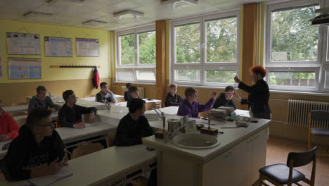 Students-Looking-At-The-Their-Teacher-Demonstrating-Scientific-Theory-In-Classroom