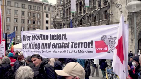 Personas-Sosteniendo-Una-Pancarta-En-Alemán-Durante-Una-Manifestación-Contra-La-Guerra-En-Munich,-Baviera,-Alemania-Leyendo-&#39;el-Suministro-De-Armas-Siembra-La-Guerra-Y-Cosecha-El-Terror&#39;