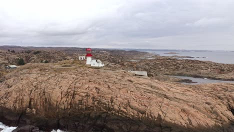 Luftaufnahme-Aus-Geringer-Höhe-Um-Den-Leuchtturm-Von-Lindesnes-Mit-Touristen,-Die-Um-Museumsgebäude-Herumlaufen-–-Dramatische-Wolken-Und-Nordseehintergrund-–-Südnorwegen