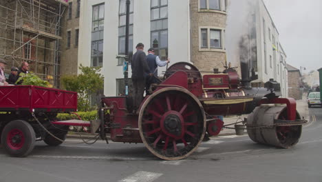 Dos-Hombres-Conducen-Un-Rodillo-Compactador-De-Vapor-Con-Remolque-En-La-Calle-Durante-El-Día-De-Trevithick-En-Camborne,-Inglaterra,-Reino-Unido.