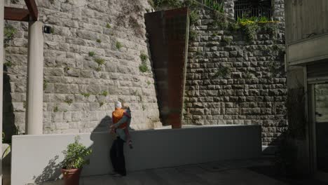 A-mother-with-her-child-looking-at-a-fountain-next-to-historic-walls-in-Trieste,-Italy