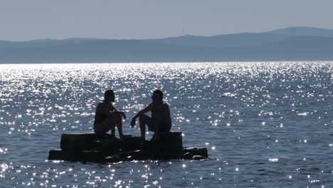 A-couple-sitting-and-chatting-on-a-small-rock-formation-in-the-middle-of-a-shimmering-Adriatic-Sea