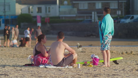 Charlando-En-Familia-Mientras-Come-En-La-Playa-De-Perranporth,-Cornualles,-Después-De-Nadar-En-El-Océano