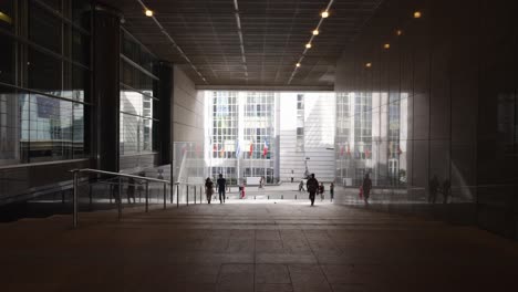 Wide-angle-of-person-silhouettes-walking-through-the-corridor-tunnel-of-the-European-Parliament-in-Brussels,-Belgium