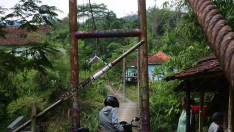 suspension-bridge-over-the-river-with-motorcycle-crossing-on-it-in-the-morning-in-Sukabumi,-west-java,-Indonesia-on-May-4,-2022