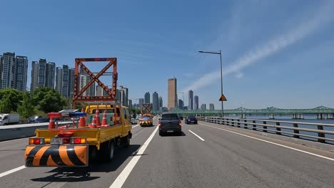 Vehicles-Passing-By-Highway-Maintenace-Truck-Parked-At-Olympic-Daero-Highway-Along-The-Han-River-In-Seoul,-South-Korea