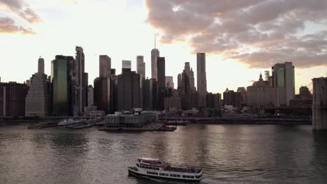 Vista-Aérea-Sobre-Un-Ferry-En-El-Río-Este-Frente-Al-Horizonte-Inferior-De-Manhattan,-Puesta-De-Sol-En-Nueva-York,-Estados-Unidos---Aumento,-Disparo-De-Drones