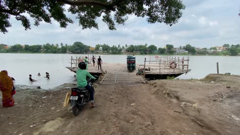 Video-of-a-small-wooden-ferry-with-a-crowd-of-passengers-and-vehicles-at-a-harbor-to-cross-a-river-in-the-town-of-Murshidabad,-India