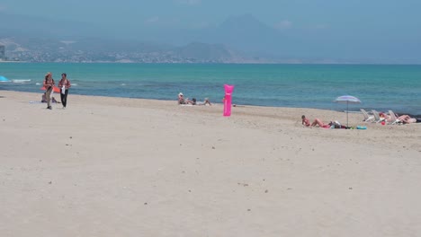 People-sunbathe-while-lying-down-at-the-beach-on-the-shore-of-the-Mediterranean-sea-in-Alicante,-Spain