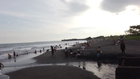 Los-Balineses-Indonesios-Se-Bañan-En-La-Playa-Local-De-Arena-Negra-Y-Cielo-Nublado,-En-La-Playa-De-Luna-Llena,-Sukawati,-Gianyar,-Bali,-Sudeste-Asiático