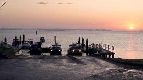 Zeitraffer-Einer-Bootsrampe-Bei-Sonnenaufgang,-Während-Autos-Und-Boote-Rückwärts-Die-Rampe-Hinunterfahren,-Um-Ihr-Boot-Zu-Wasser-Zu-Lassen