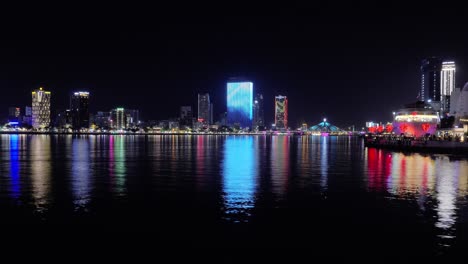 Ciudad-De-Da-Nang-En-El-Centro-Por-La-Noche,-Vietnam,-Vista-Panorámica-Del-Río-Han,-Edificios-Y-Torres-Iluminados,-Barcos-Que-Navegan,-Turistas-En-El-Famoso-Destino-Turístico-Love-Pier