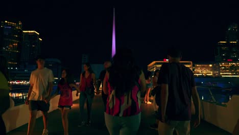 Group-of-tourists-walking-along-the-Women's-Bridge-at-night-in-Puerto-Madero,-Buenos-Aires,-Argentina