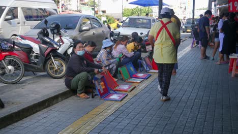 Foto-De-Un-Grupo-De-Señoras-Sentadas-En-La-Acera-Vendiendo-Billetes-De-Lotería-A-Lo-Largo-De-La-Carretera-En-La-Provincia-De-Songkhla,-Tailandia-Durante-El-Día