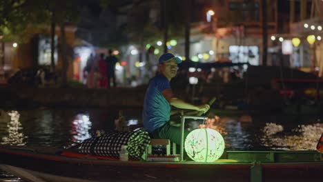 Vietnamesischer-Mann,-Der-Nachts-Ein-Von-Einer-Laterne-Beleuchtetes-Paddelboot-In-Hoi-An,-Vietnam,-Beleuchtet